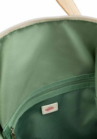 Groene nylon tas binnenkant met een gladde textuur, een meshvak en een klein wit etiket met de tekst "oilily." Ritsluiting aan de bovenkant.