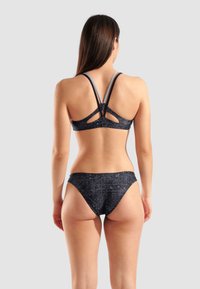 Zwart bikini set met een geperforeerde bralette met een uitgesneden achterkant en smalle bandjes, gecombineerd met low-rise bikini broekjes met zijstrik.