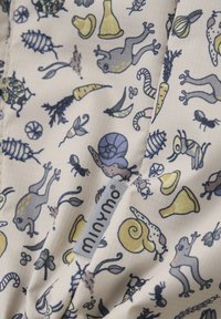 Mönstrat tyg med illustrationer av grodor, sniglar, insekter och grönsaker i mjuka färger av kräm, blått och gult; varumärkesetikett synlig.