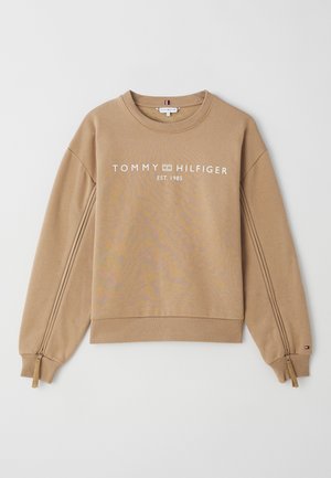 Sudadera marrón claro con mangas largas, puños acanalados y escote redondo. Presenta un logotipo en texto blanco en la parte frontal y detalles con cremallera en las mangas.