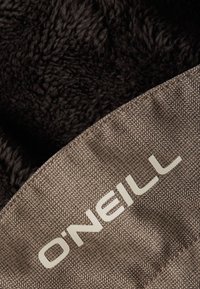 Bruine visgraatstof met een donzige zwarte textuur eronder. Kenmerkt zich door een wit "O'Neill" logo dat op de rand is geborduurd.