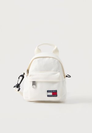 Kleiner weißer Canvas-Rucksack mit vorderer Reißverschlusstasche, schwarzem Clip an der Seite und Tommy Jeans Logo-Patch auf der Tasche.