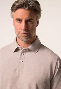 Světle béžové polo tričko vyrobené z měkké bavlny, s klasickým límečkem, třemi knoflíky a hladkým, strukturovaným povrchem.