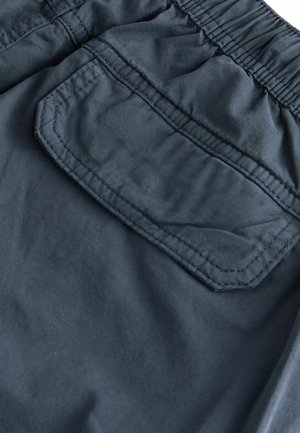 Shorts de tejido azul marino oscuro con cintura elástica, pliegues laterales y un bolsillo trasero con parche y detalles de costura en contraste.