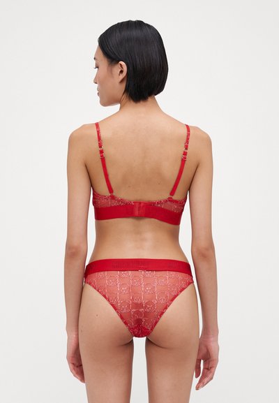 Sarkans mežģīņu bralets un saskaņoti bikini ar logo joslu. Iezīmē regulējamas siksnas, caurspīdīgu tekstūru un ziedu rakstu ar reljefa detaļām.