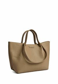 Beige nahkakassi, jossa on kaksi ylhäällä olevaa kantohihnaa, jossa on sileä pinta, pyöristetyt reunat ja suuri brändilogo edessä.