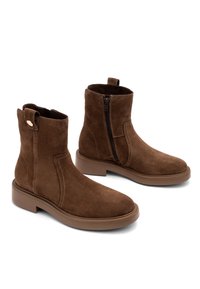 Brązowe zamszowe botki za kostkę z bocznym zamkiem błyskawicznym, okrągłym noskiem i płaską, teksturowaną gumową podeszwą. Pętla z tyłu ułatwiająca zakładanie.