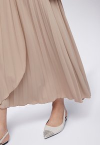 Gonna beige plissé con un design fluido, abbinata a scarpe slingback bianche appuntite con dettagli a borchie sulla punta.