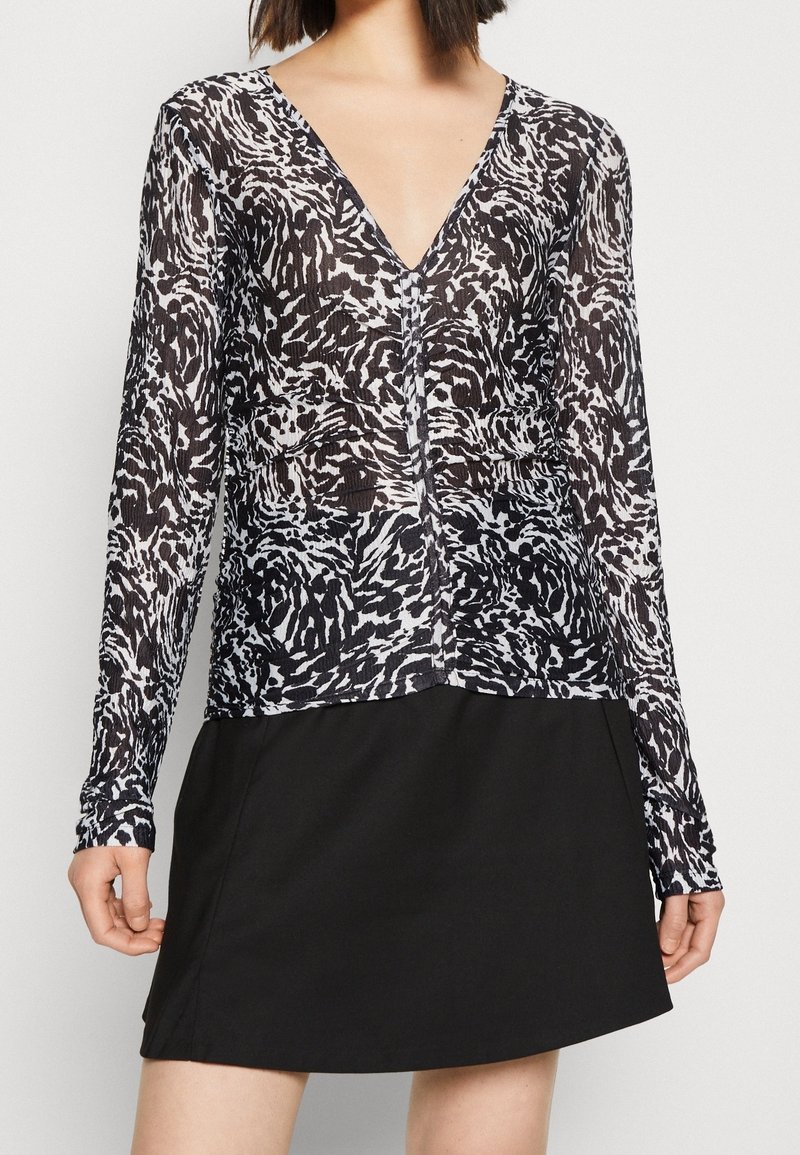 Schwarz-weiß gemusterte langärmlige Bluse mit tiefem V-Ausschnitt, weichem Material und tailliertem Schnitt, kombiniert mit einem einfachen schwarzen Rock.