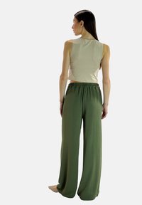 Beige cropped tanktop en losse, olijfgroene broek met een elastische tailleband, van achteren getoond tegen een effen achtergrond.