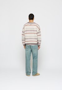 Prugasta pulover s pastelnimi barvami, okroglo izrezano ovratnico in sivo obrobo na dnu. Nosi se z svetlo modrimi kavbojkami in svetlo rjavimi čevlji.