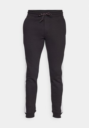 Pantalons de survêtement noirs avec une taille à cordon de serrage, présentant des panneaux latéraux gris, des bords côtelés aux chevilles et une texture lisse.