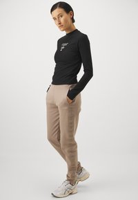 Sort langærmet skjorte med hvidt logo, parret med beige sweatpants med side-logoer og lommer. Model iført lyse sneakers.