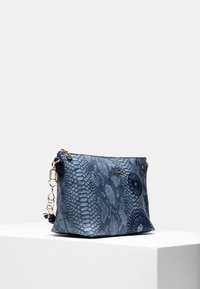 Niebieska torebka o fakturze skóry węża i okrągłych, przeszywanych wzorach, z złotym zamkiem błyskawicznym i zapięciem, prezentowana na białym postumencie na szarym tle.