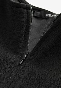 Giacca nera con zip e una superficie testurizzata. Presenta un colletto rotondo e un cursore della zip liscio, realizzata in tessuto morbido.