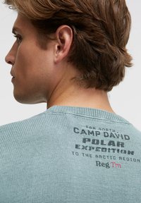 Hellblauer Strickpullover mit rundem Kragen und sichtbarer Textur. Rückendetail mit dem Schriftzug "CAMP DAVID POLAR EXPEDITION."