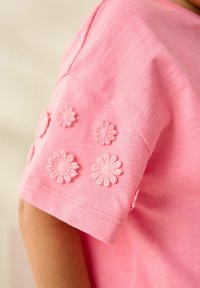 Roze katoenen t-shirt met geborduurde bloemdetails op de mouwen en een gladde textuur. Korte mouwen met decoratieve accenten.