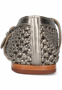 Zapato tejido de color plata metálico con tacón plano, patrón de tejido abierto, ribete de cuero y suela de madera lisa. Cuenta con una correa trasera para mayor soporte.