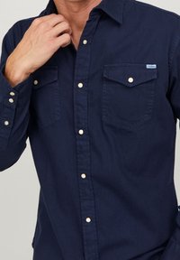 Camicia button-up di cotone blu navy, con due taschini sul petto, colletto a punta e bottoni chiari. Texture morbida con un design classico.