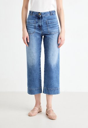 Hellblaue weit geschnittene Jeans mit hoher Taille, ausgestattet mit zwei Vordertaschen, einem Knopfverschluss und umgeschlagenen Säumen. Getragen mit flachen Schuhen in Blush-Farbe.