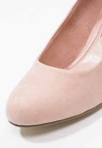 Escarpin en suede rose avec un bout arrondi, doublure intérieure lisse et un léger éclat sur la semelle. La texture est douce et mate.