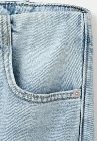 Lyseblåt denimstof med en topstitched lomme kant og en lille sølvnitte på højre side nær sømmen.