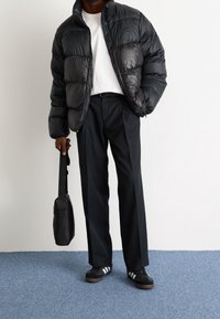 Black puffer jacket with shiny finish, white t-shirt, black trousers, and black sneakers with white stripes. Carrying a small black bag.