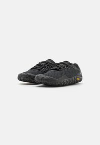 Black athletic shoes with a textured mesh upper, featuring a rubber sole with a patterned grip and contrasting yellow branding on the side.