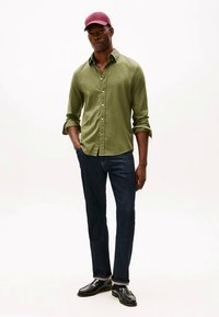 Olivengrøn skjorte med knapper, mørke jeans og sorte loafers, suppleret med en mørkerød kasket. Elegant design med opsmøgede ærmer og lige pasform.