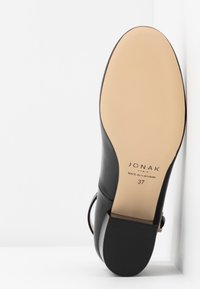 Semelle de chaussure en cuir noir avec semelle beige, talon carré, et "JONAK Paris Made in Portugal 37" imprimé sur la semelle.