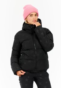 Zwarte pufferjack met een sterrenpatroon, met een hoge kraag, ritszakken en een aansluitende zoom. Gecombineerd met een gestructureerde roze gebreide beanie.