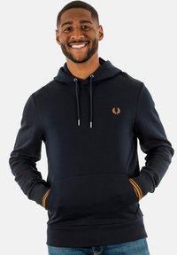 Sudadera con capucha de color azul marino en tejido suave, con un bolsillo frontal, logo dorado y acentos de rayas naranjas en los puños.