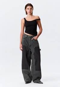 Μαύρο αμάνικο τοπ συνδυασμένο με oversized γκρι τζιν που διαθέτουν σκούρα υφασμάτινα πάνελ, πλαϊνές τσέπες και ασημένιες λεπτομέρειες.