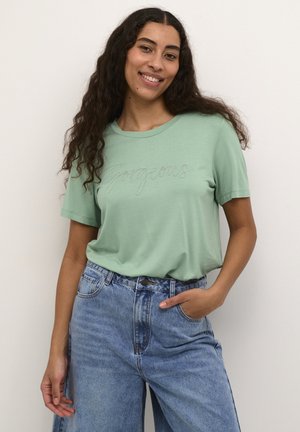 Lys grøn bomulds t-shirt med korte ærmer og "Gorgeous" broderet i sølvtråd, parret med højtaljede blå denim jeans.
