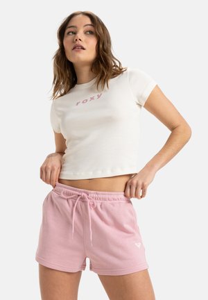T-shirt bianco corto con logo "roxy" rosa, abbinato a pantaloncini rosa chiaro con cordino, dotati di un piccolo emblema bianco sull'orlo.