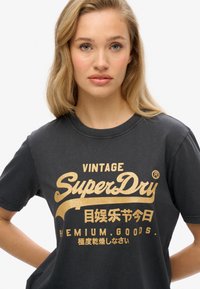 Zwarte katoenen t-shirt met gouden tekst "VINTAGE SuperDry PREMIUM GOODS" en extra graphics en tekens. Klassiek crew neck ontwerp.