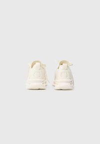 Une paire de baskets lacées blanc cassé vues de l'arrière sur un fond clair.