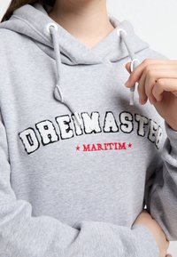 Grijze hoodie met een frontlogo met witte letters in reliëf en rode accenten. Het heeft een capuchon met trekkoord en geribbelde manchetten.