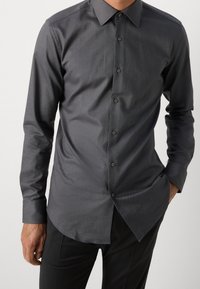 Donkergrijs overhemd met knopen, gemaakt van gladde stof, met een klassieke kraag, lange mouwen en een licht getailleerde pasvorm met een afgeronde zoom.