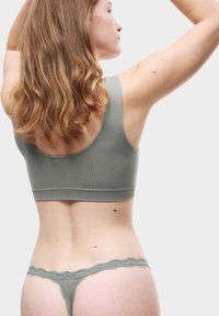 Grå sömlös bralette med breda axelband, kombinerad med grön thong med spetskant. Slät textur, åtsittande design, visar en bakvy.