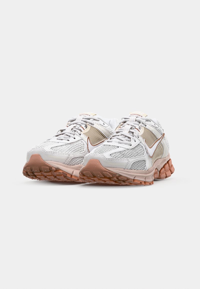Lichte hardloopschoenen met een witte mesh bovenkant, crèmekleurige accenten en een gestructureerde, rubberen, roze-bruin zool. Kenmerkt zich door opvallende veters en branding.