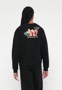 Sudadera negra con un gráfico colorido en la parte posterior con acentos florales y el texto "Riviera PROJECTS". Tejido suave, corte relajado.