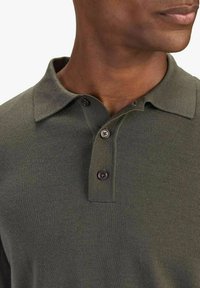 Donkergroene polo shirt van gebreid stof, met een kraag, twee bruine knopen en een subtiel gemêleerd patroon. Close-up weergave.