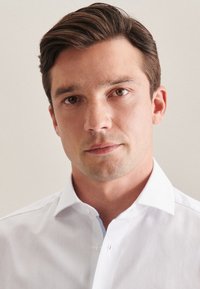 Biała koszula z klasycznym kołnierzykiem i zapięciem na guziki. Jasnoniebieski akcent pod kołnierzykiem. Gładka, wyraźna faktura materiału.