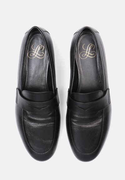 Paire de mocassins noirs en cuir pour hommes avec détail de bride et monogramme doré à l'intérieur, vus de dessus sur fond blanc.