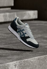 Γκρι και ναυτικές αθλητικές παπούτσια με πλέγμα και σουέτ υλικά, στρογγυλή μύτη, λευκή σόλα και επίπεδο σχέδιο με μπλε λεπτομέρειες.