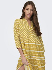 Žuta haljina s bijelim cik-cak i geometrijskim uzorcima, s tričetvrtinim rukavima i slojevitom konstrukcijom, izrađena od lagane tkanine.