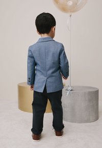 Blue checkered blazer with a single vent, paired with dark pants and brown shoes. A gold balloon and cylindrical surfaces in background.