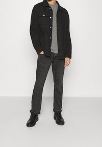 Sort denimjakke over en grå t-shirt, kombineret med mørke jeans og sorte ankelstøvler. Jakken har sølvfarvede knapper og lommer.