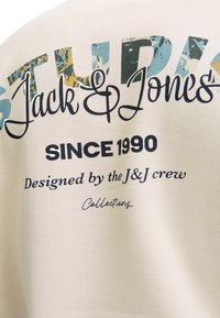 Tessuto bianco con testo colorato stampato: "STUDIOS Jack & Jones SINCE 1990 Designed by the J&J crew Collections."